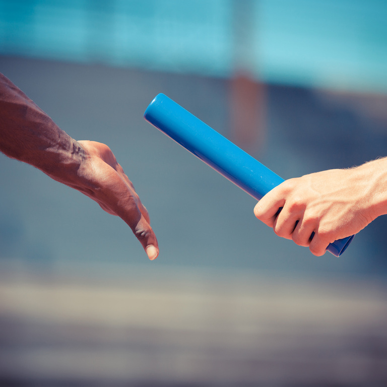 Two relay runners working together to complete a baton handoff