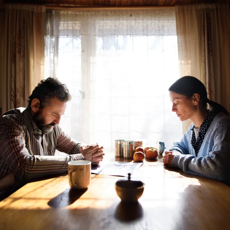 Entrepreneur sitting at a kitchen table with a laptop pushed aside, talking with their spouse over coffee.