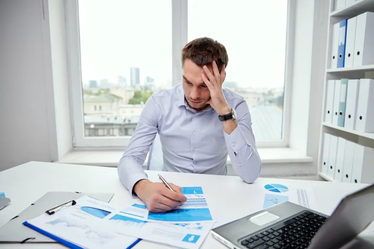 A small business owner feeling overwhelmed by financial stress, surrounded by bills and paperwork.