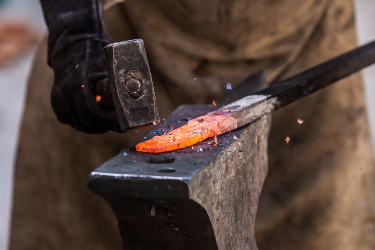 a smithy forges a sword striking a red-hot with a forge hammer