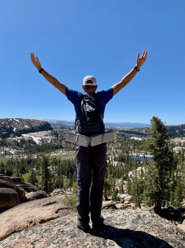 A man standing at the edge of a mountain overlook at sunrise, looking out with peace and clarity toward the horizon.