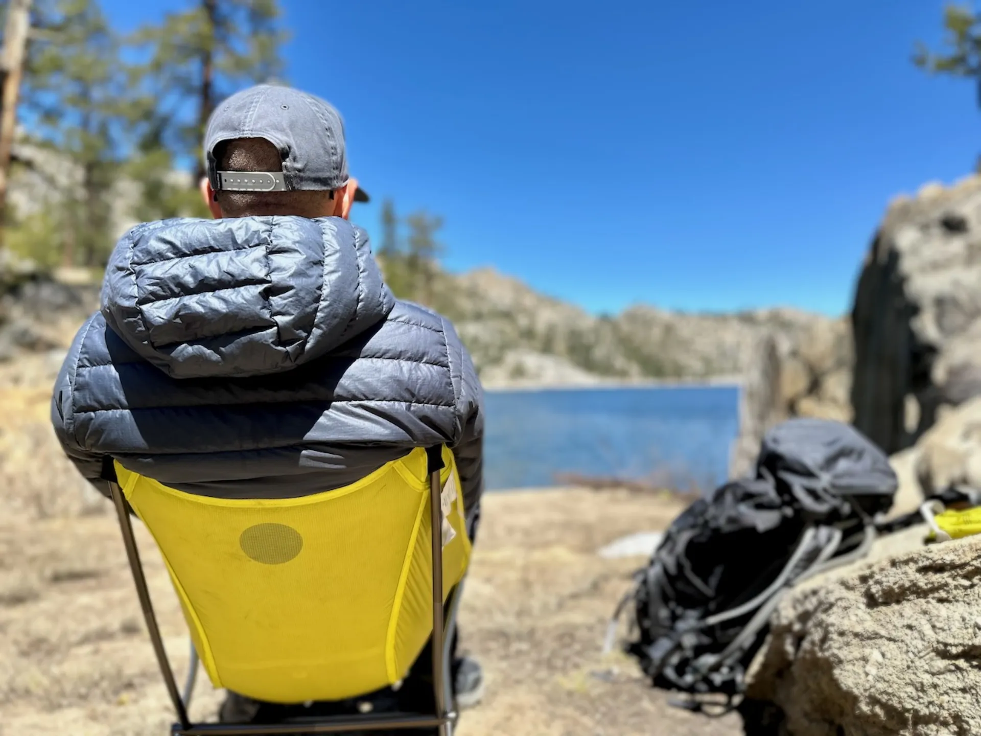 A man sitting alone by a quiet mountain lake, completely off-grid and unplugged.