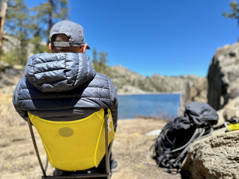 A man sitting alone by a quiet mountain lake, completely off-grid and unplugged.