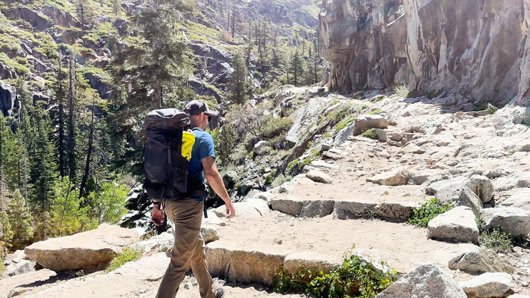 A man hiking along a quiet mountain trail, surrounded by rugged wilderness.