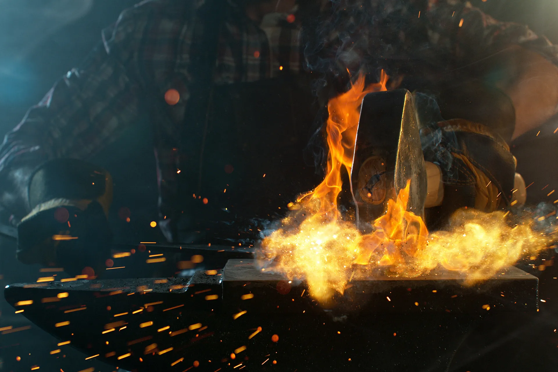 A smithy works a hot, flaming piece of steel with a forge hammer